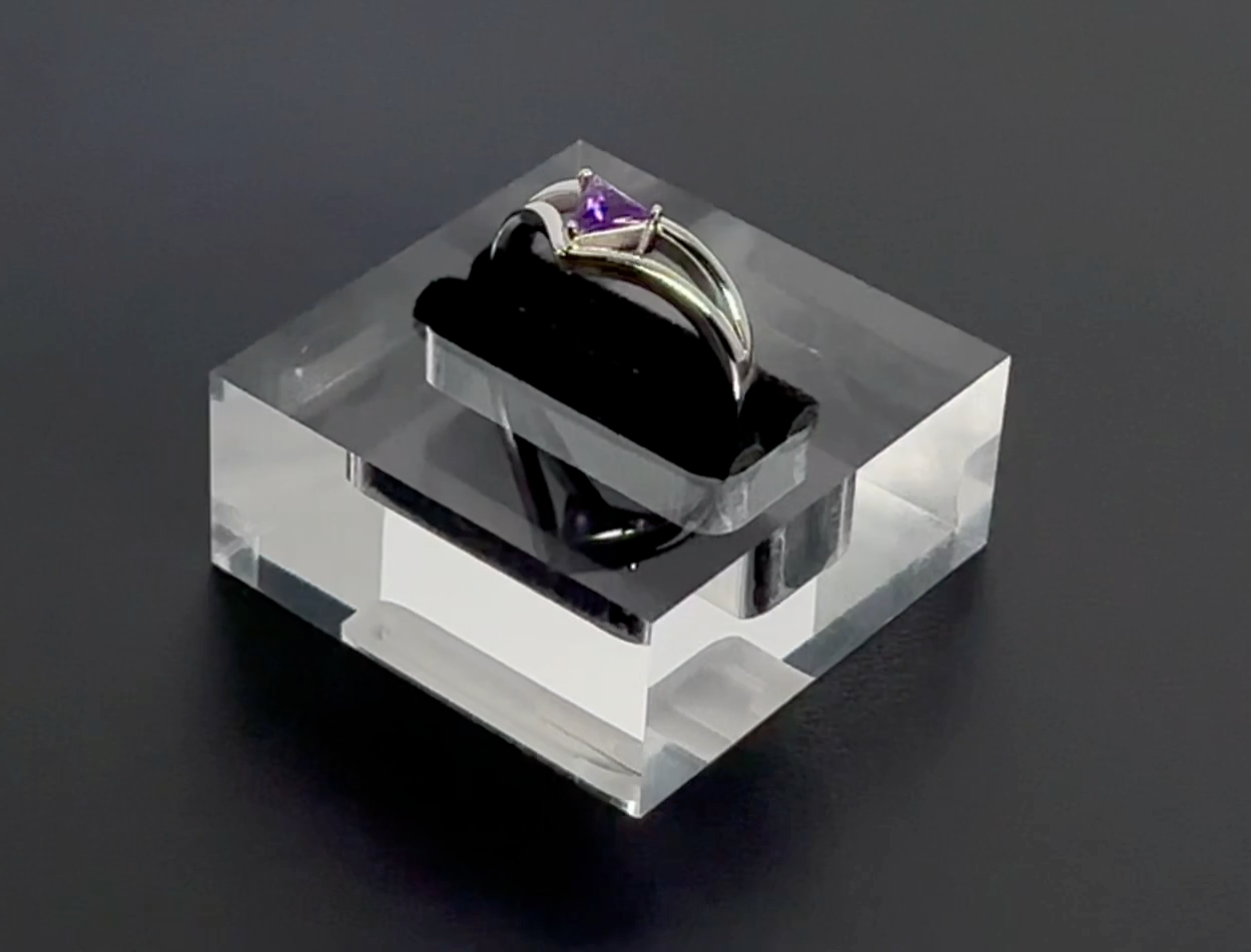 Ring with a purple gemstone on a clear stand against a dark background