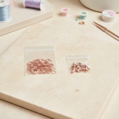 Rose gold-tone jump rings and lobster claw clasps on a bright creative workspace background